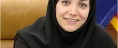 A woman in a black hijab smiling in front of flags.
