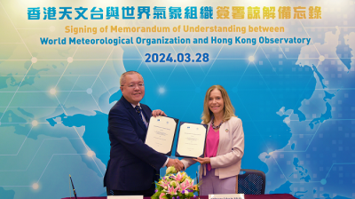 Two individuals exchanging a signed memorandum at a ceremony with a backdrop displaying logos of the world meteorological organization and hong kong observatory.