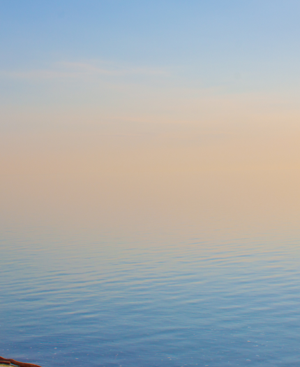 Serene lakeside view at sunset with a calm blue water and a gradient sky transitioning from blue to orange.