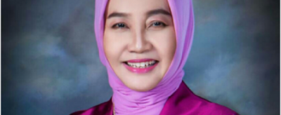 A woman wearing a purple hijab smiles for the camera.