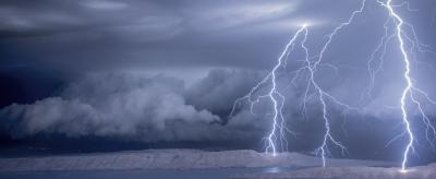 Dramatic night scene with multiple lightning strikes over a calm body of water and distant mountains under a cloudy sky.