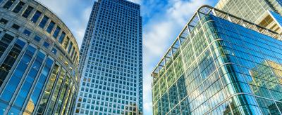 Tall glass skyscrapers under a partly cloudy blue sky, photographed from a low angle, highlighting modern architecture.