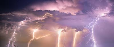 A dramatic sky with multiple lightning bolts striking across a landscape, illuminating clouds and revealing city lights below.