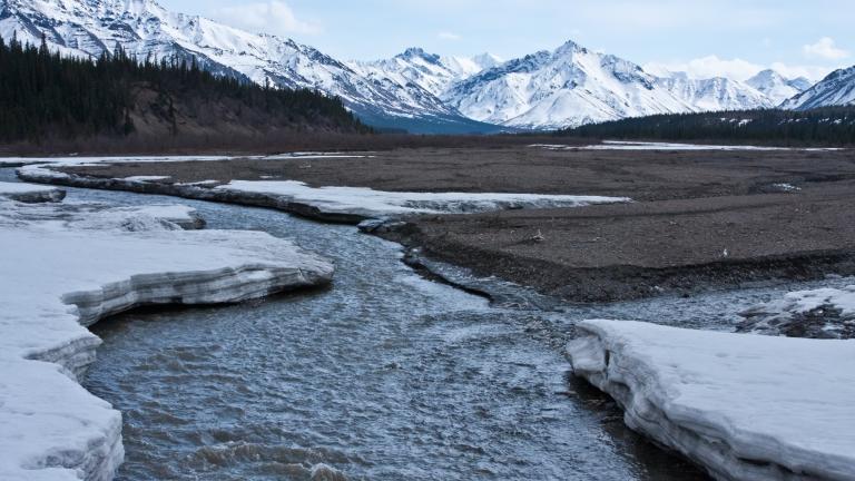 A river in the snow with mountains in the background.