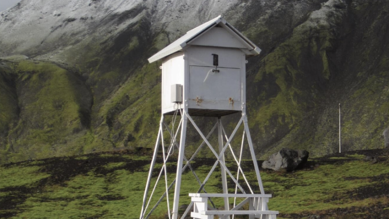 A white watchtower sits in the middle of a field with mountains in the background.