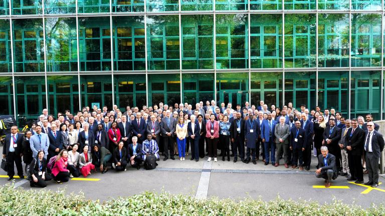 Large group of business professionals posing for a photo in front of a green glass office building.