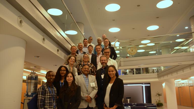 Group of diverse people smiling for a photo in a modern lobby with circular overhead lighting.
