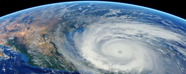 Satellite view of a large, swirling hurricane over the ocean near a continent, with a clear eye at the center and surrounding cloud bands.