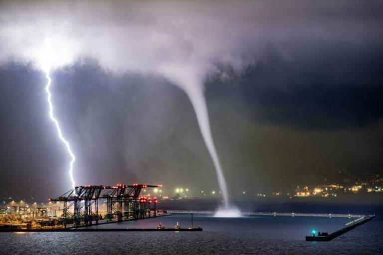 Lightning and water spout over brightly lit industrial area