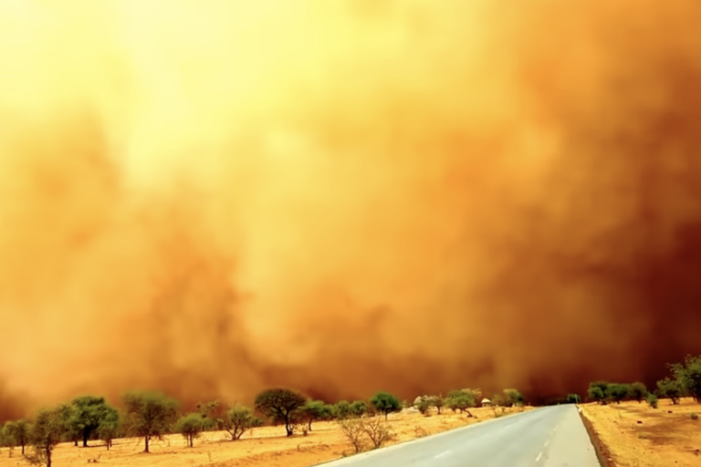 a dust storm is blowing over a road in the desert.