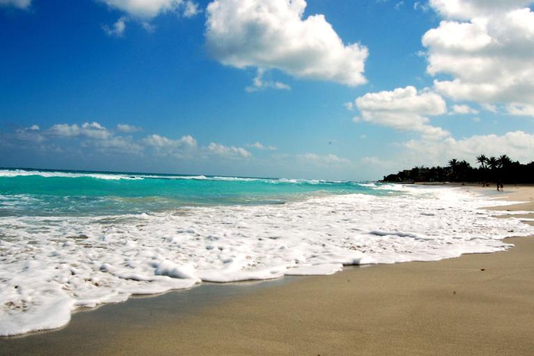 a beach with waves and clouds on a sunny day.