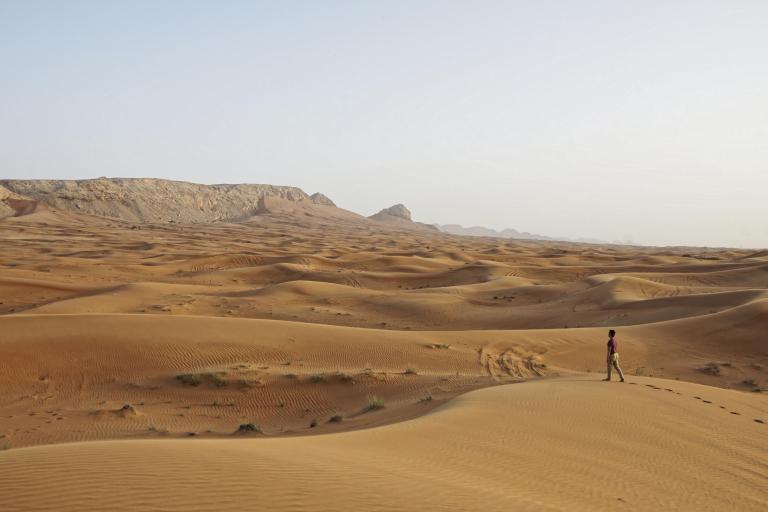 a man is walking across a desert in a sand dune.