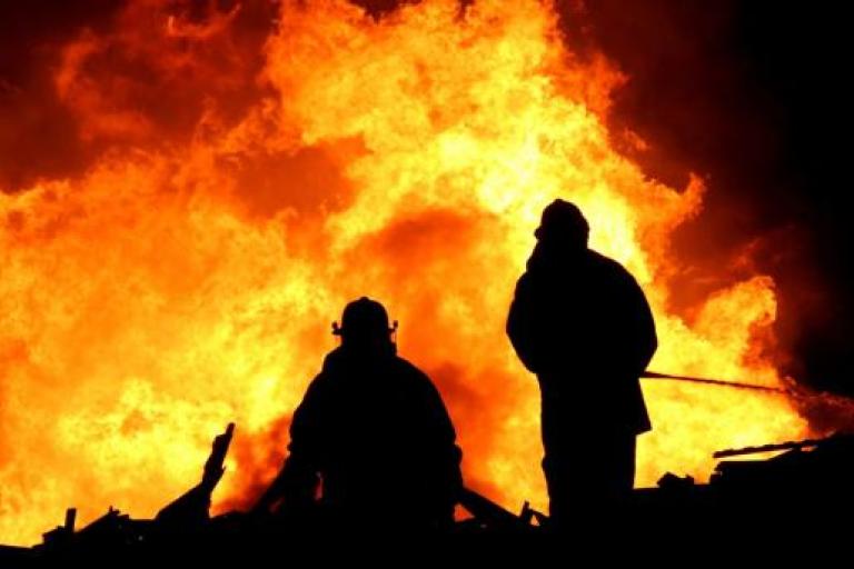 Two firefighters standing in front of a large fire.