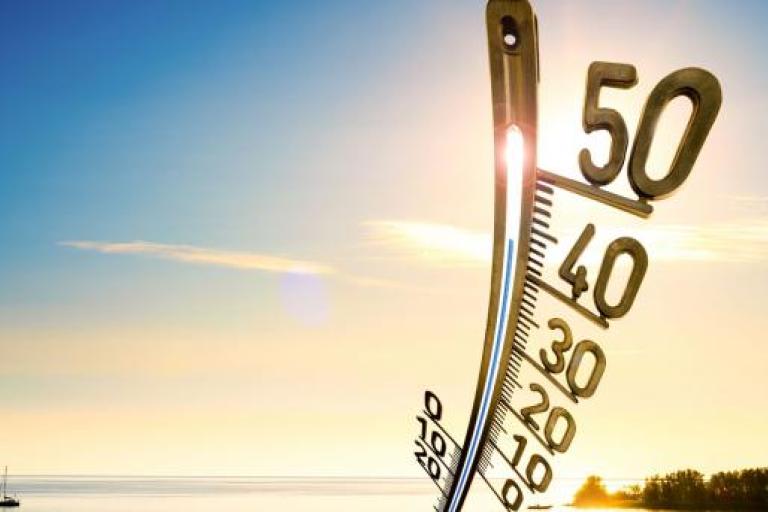 a thermometer on a beach with a boat in the background.