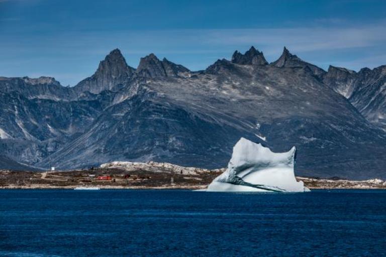 An iceberg floating in the ocean with mountains in the background.