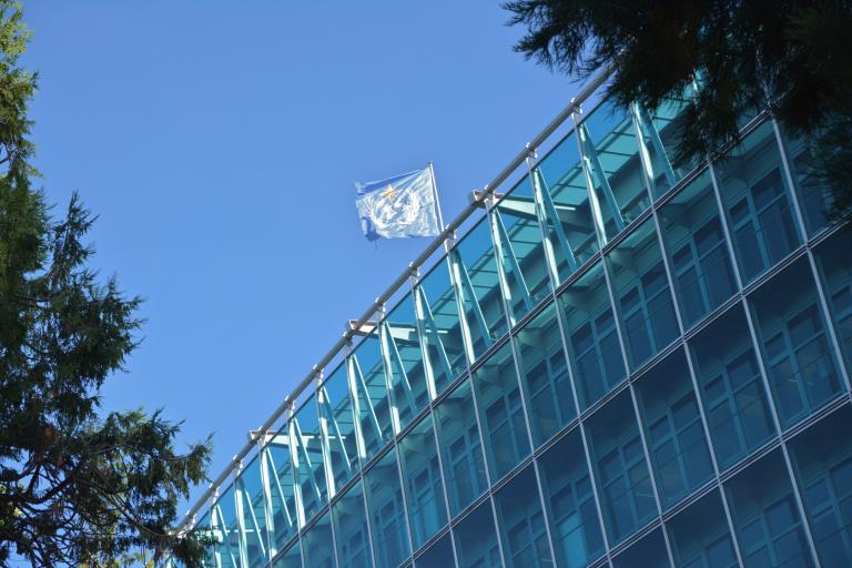 The flag of the united nations flies over a glass building.