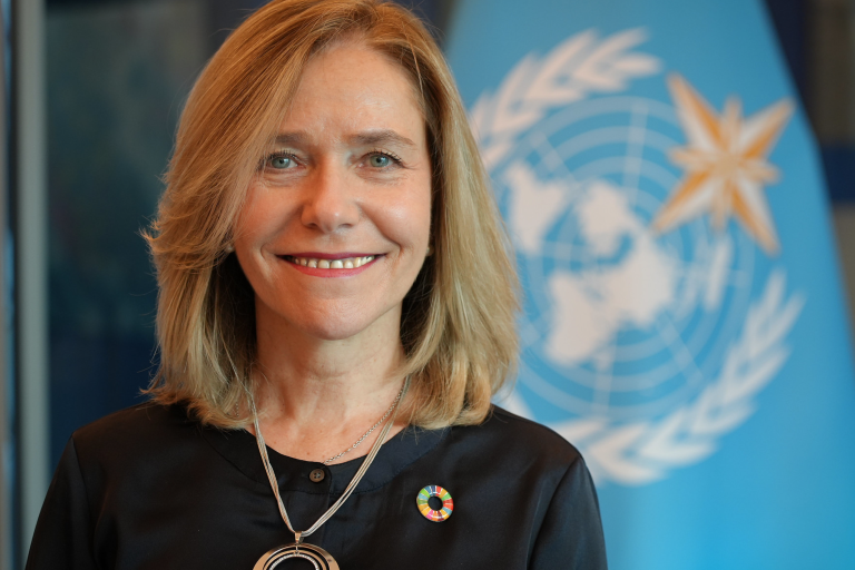 A woman smiling in front of a flag.