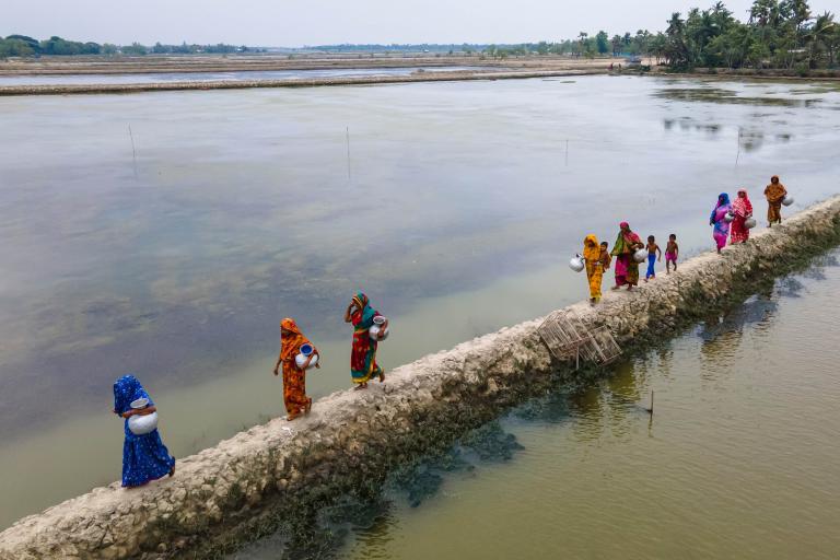 A group of women walking on a wall with water.