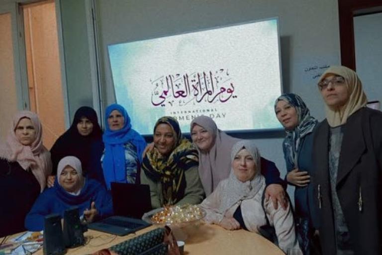 Group of women posing together in a room with a screen displaying text in the background for an event or celebration.