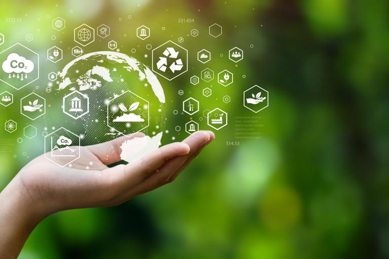 Hand holding a glowing globe with environmental icons, symbolizing eco-friendly technologies and sustainability, against a green blurred background.