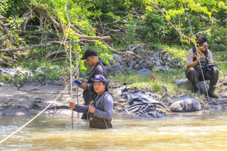 Three individuals conducting a survey in a shallow river.