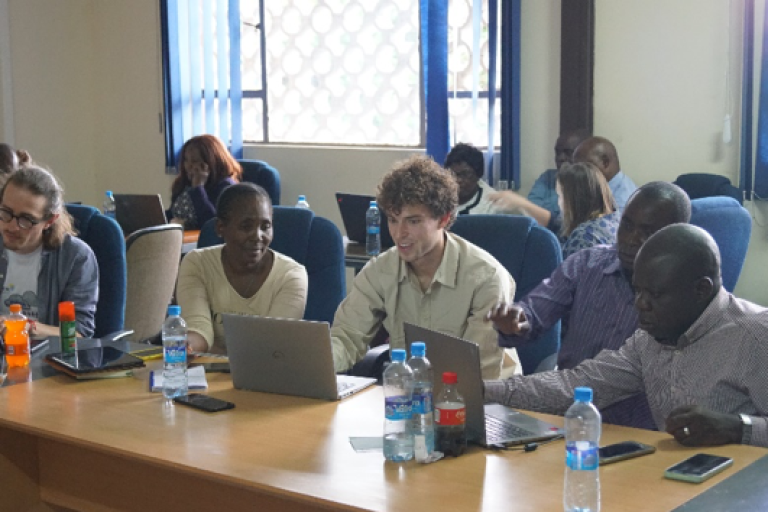 Group of adults sitting at a conference table with laptops, engaged in a discussion.