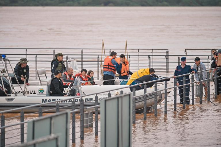 Rescue workers and divers preparing on a dock with boats on a muddy river, likely in response to an emergency.