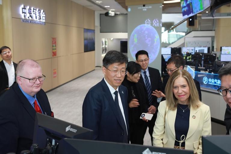 Group of professionals, including a woman and two men in the foreground, observing monitors in a high-tech control center.