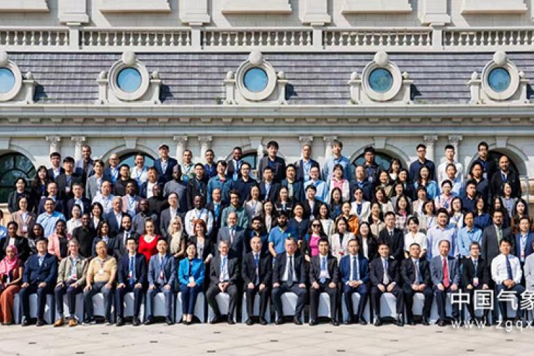A large group of diverse people posing for a formal photo in front of an elegant building with classical architecture.