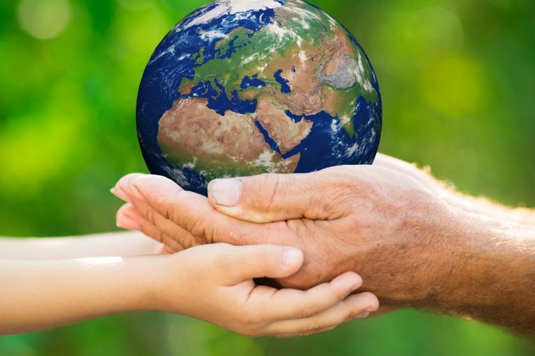Hands of an elderly person and a child holding a small globe against a blurred green background.