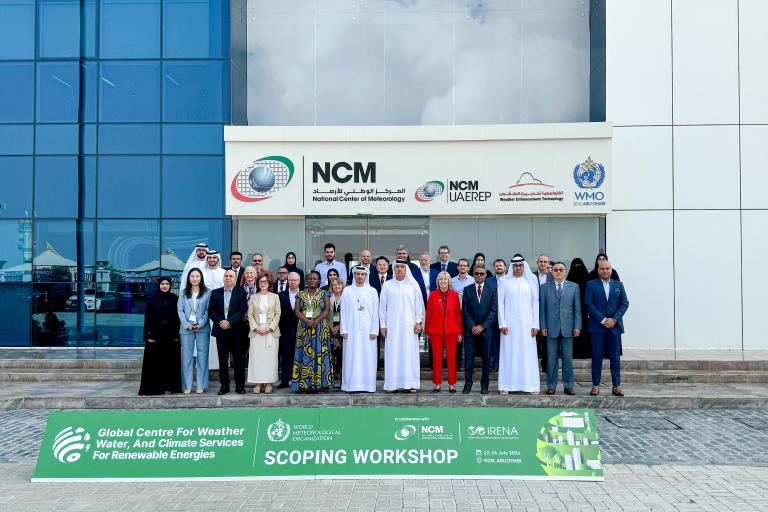 A group of people stands in front of the National Center of Meteorology (NCM) building, displaying a banner that reads "Global Centre for Weather, Water, And Climate Services for Renewable Energies Scoping Workshop.
