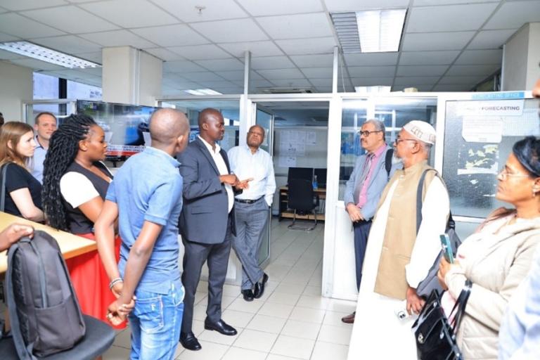 Group of people in an weather forecasting centre, with one individual in a suit speaking while others listen attentively.