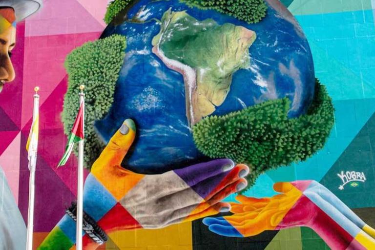 Colorful mural depicting a man and a child holding up a globe together, surrounded by vibrant geometric patterns.