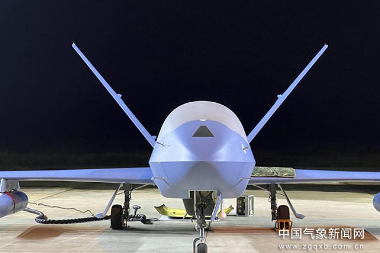 A large drone is positioned on a tarmac at night, illuminated by artificial light. Two wings are visible, along with the ground equipment and cables connected to it. Chinese text is displayed at the bottom right.