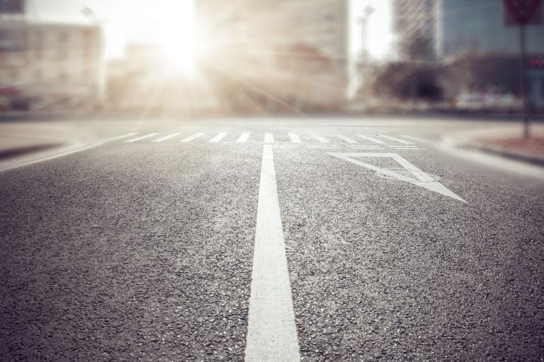 Empty city street intersection at sunrise with visible road markings, including a straight arrow and a pedestrian crosswalk.
