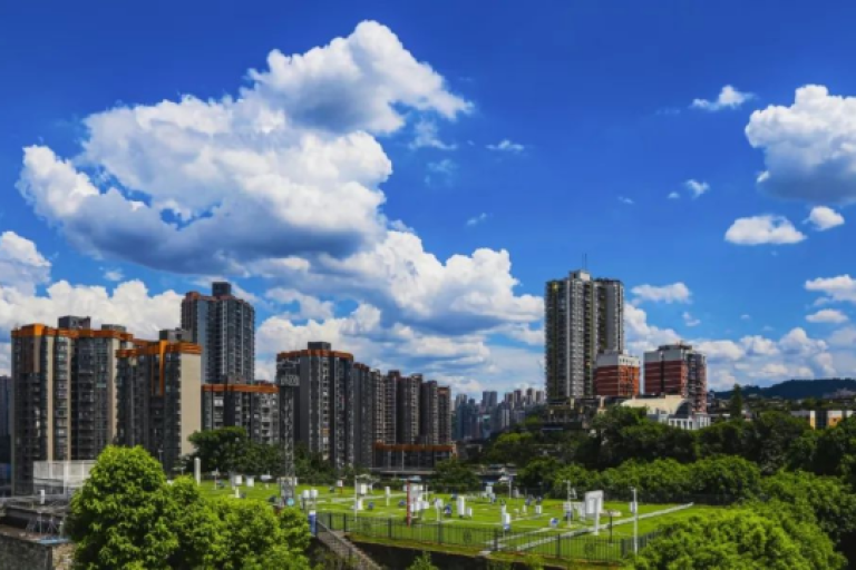 Urban skyline with tall residential buildings, green spaces, and a cemetery in the foreground under a partly cloudy sky.