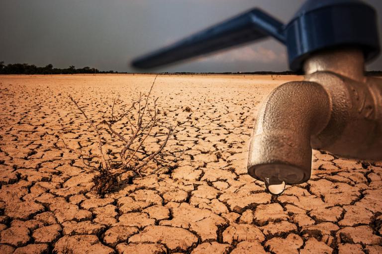A dry, cracked landscape with a single dried plant and a close-up of a faucet with a single droplet of water, symbolizing drought and water scarcity.