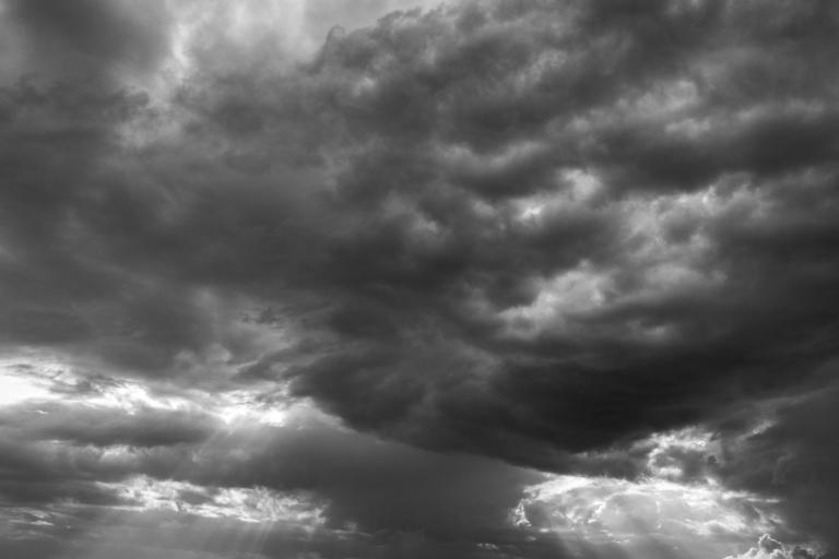Black and white photo of a sky filled with dark, dramatic clouds, with some light breaking through at the edges.