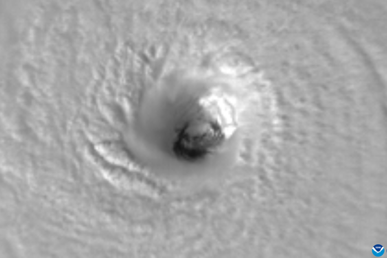 Satellite image of a hurricane's eye viewed from above, showing swirling cloud patterns.