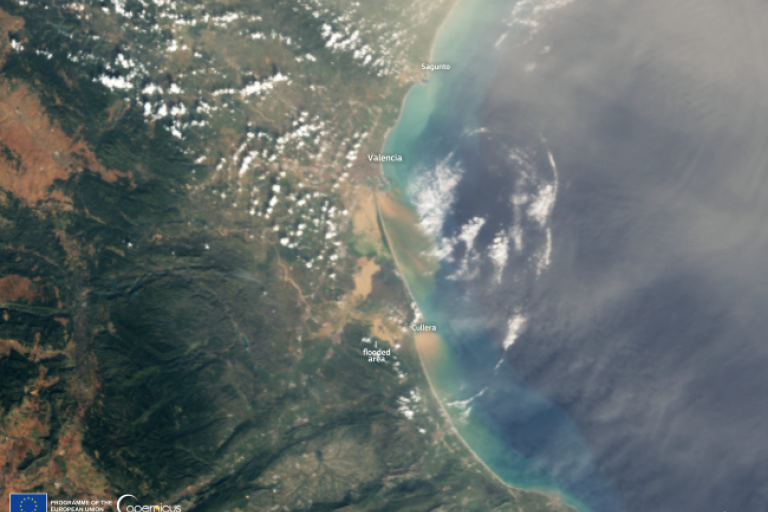 Satellite image showing the eastern coast of Spain, including Valencia, a flooded area, and labeled cities, with a mix of land, clouds, and ocean.