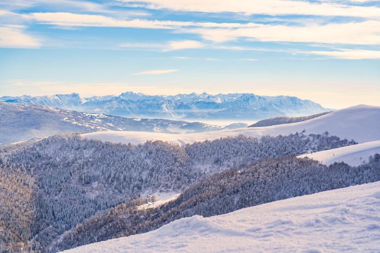 Snow-covered mountains and forested hills under a clear blue sky with distant peaks in the background.