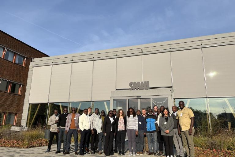 A group of people stands in front of a building labeled "SMHI" on a sunny day. The building has large windows and a concrete exterior.