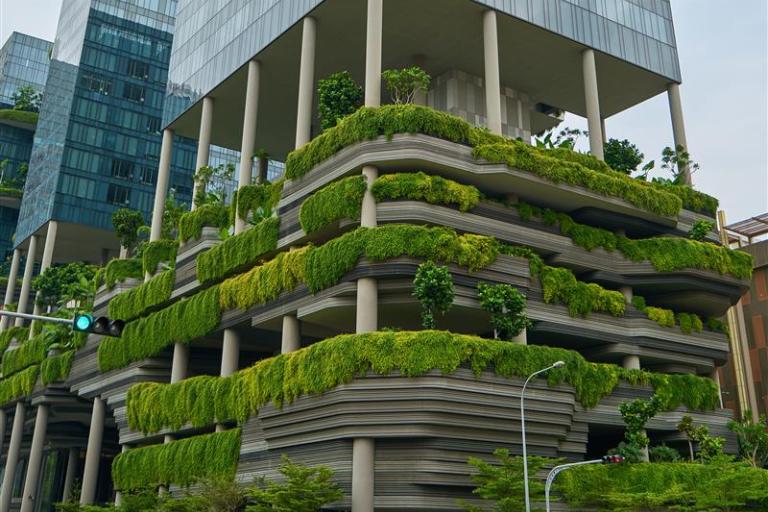 A modern building with tiered green terraces and abundant plants, featuring a blend of glass and concrete architecture.