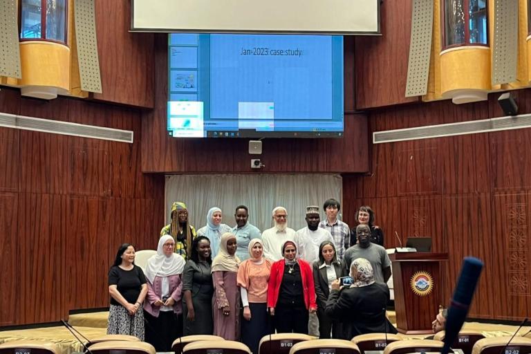 A group of people poses for a photo in front of a large screen displaying "Jan-2023 case study" in a wood-paneled auditorium.