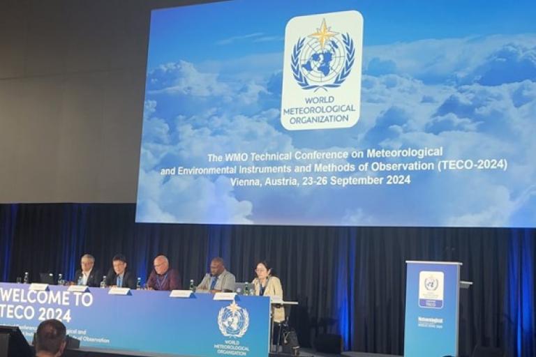 Panelists sit at a long table in front of a large screen at the WMO Technical Conference on meteorological instruments, Vienna, 2024.
