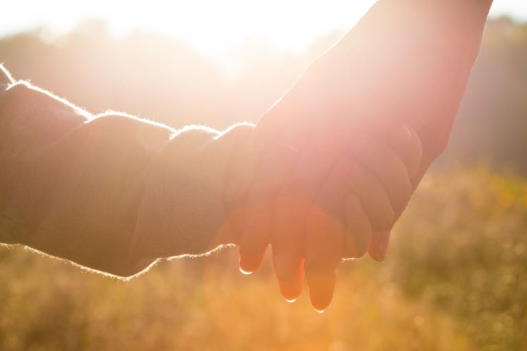 Two people holding hands with a bright sunlit background.