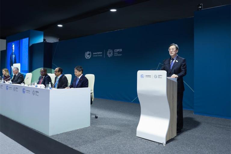 A person speaks at a podium on a stage with six seated individuals at a climate conference, featuring a blue backdrop displaying "COP28" and the UN logo.