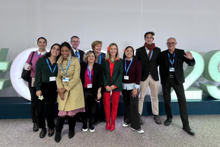 A group of ten people standing in front of large, stylized numbers and letters. Some are smiling, and they all have lanyards around their necks.