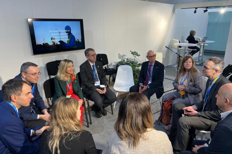 A group of people in business attire sit in a circle having a discussion in a conference room.