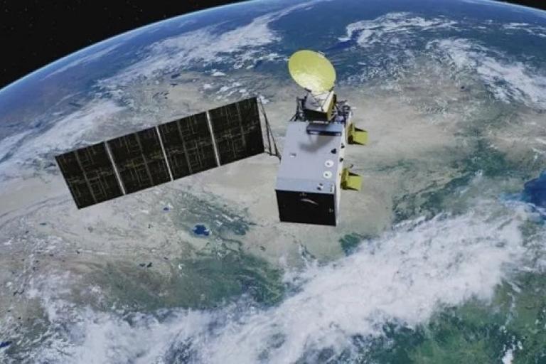 A satellite with solar panels orbits Earth, with a view of continents and clouds below.
